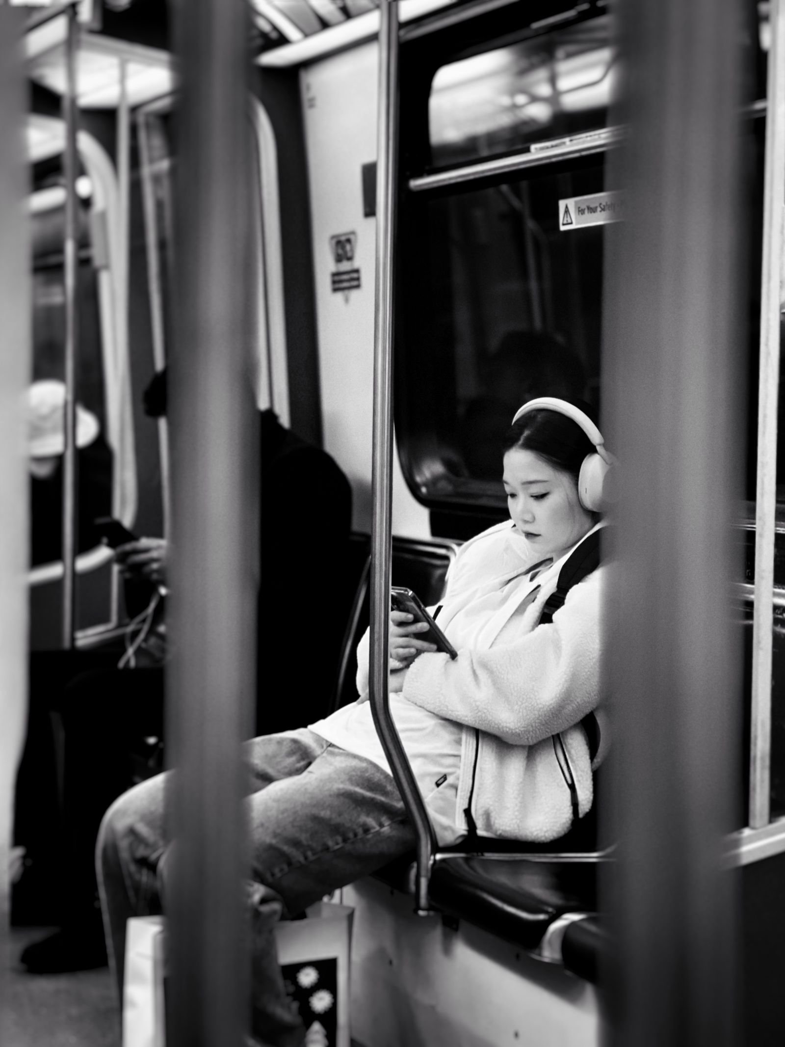 A passenger wearing headphones and looking at a phone on a train