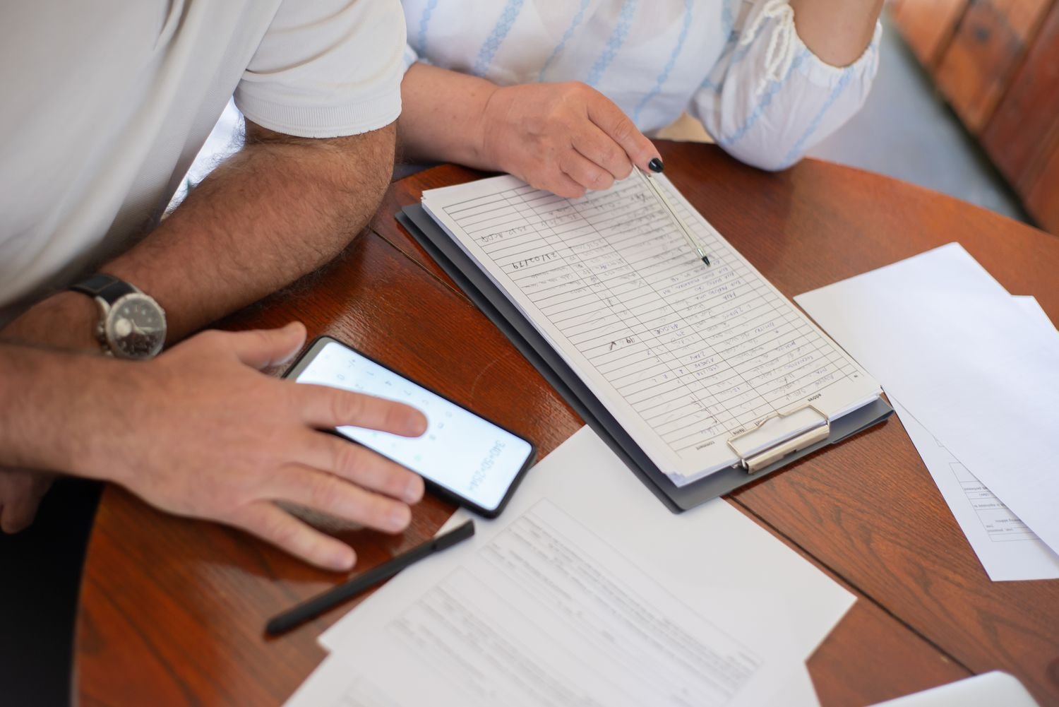 Two people checking documents with a smartphone at a table